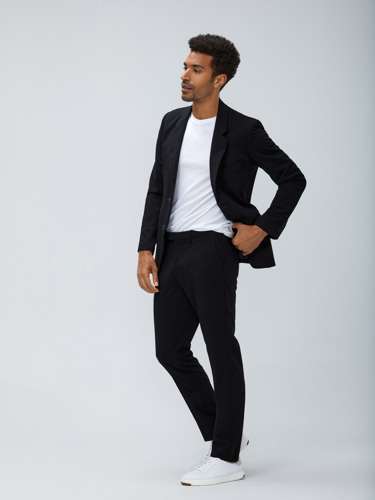 Men's Black Velocity Blazer and Black Velocity Pant with Men's White Atlas Crew Neck Tee on Model facing left adjusting waistband