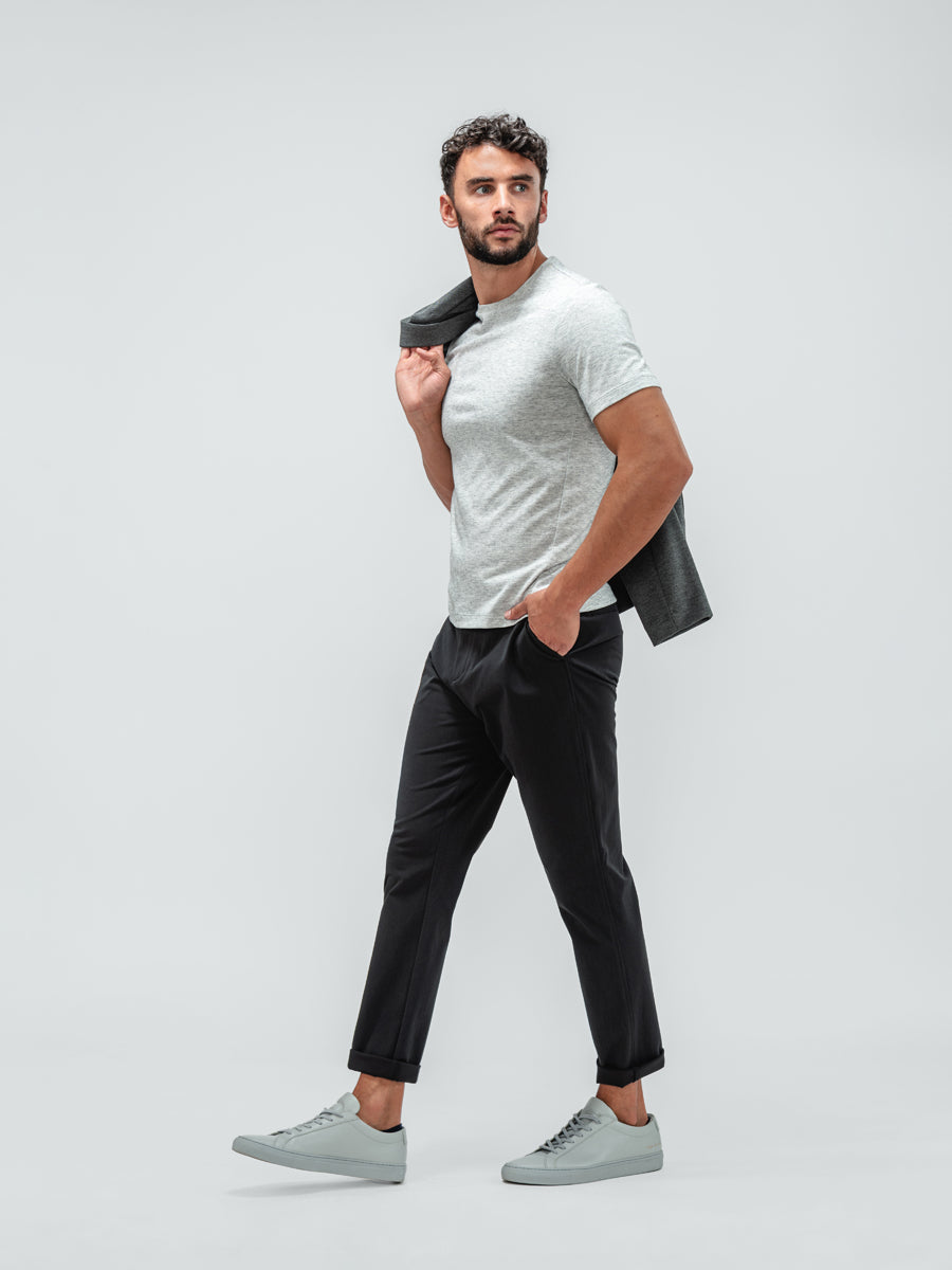 Man wearing the Momentum Tapered Chino Black, Composite Short Sleeve Tee Pale Grey Heather, and Fusion Chore Coat Charcoal with grey sneakers