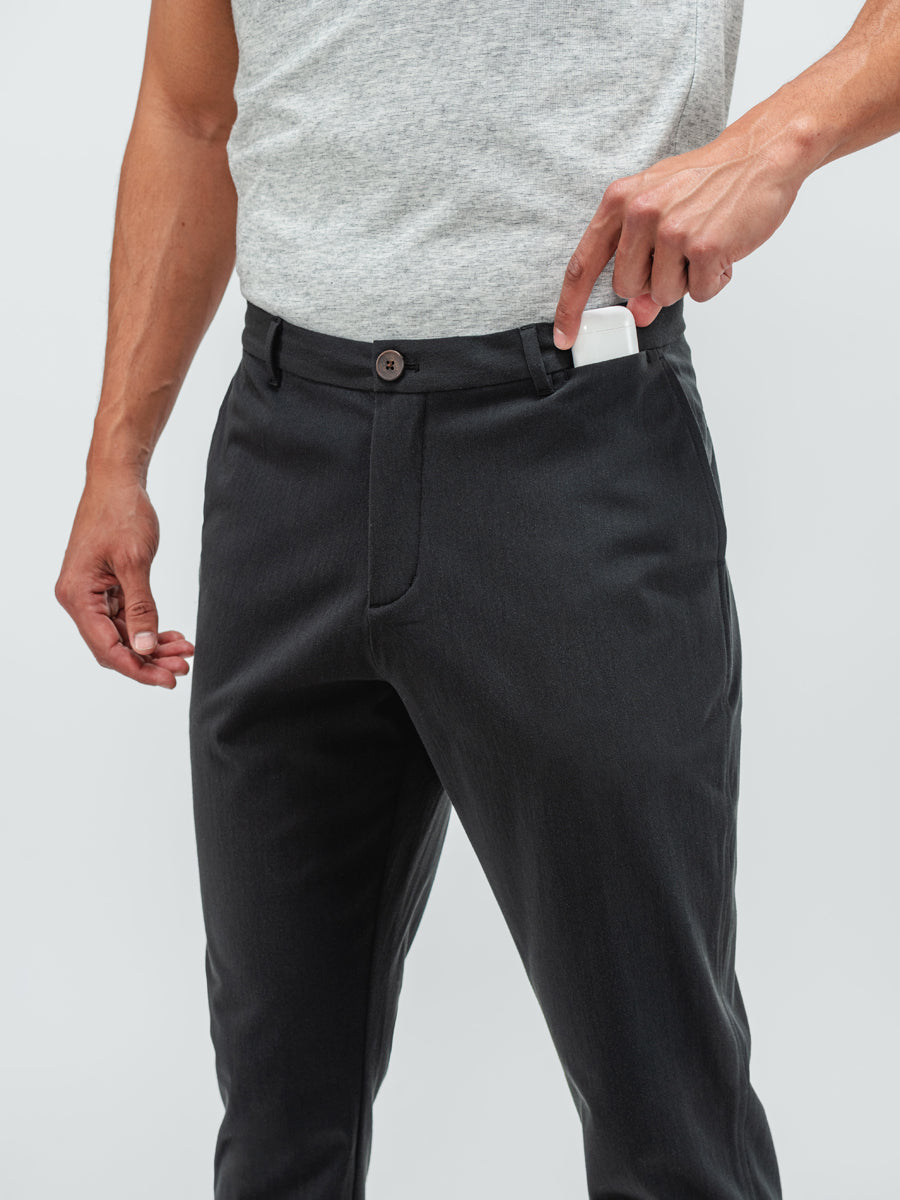 Close up of a man wearing the pace tapered chino in black and putting an ipod case in a small front pocket