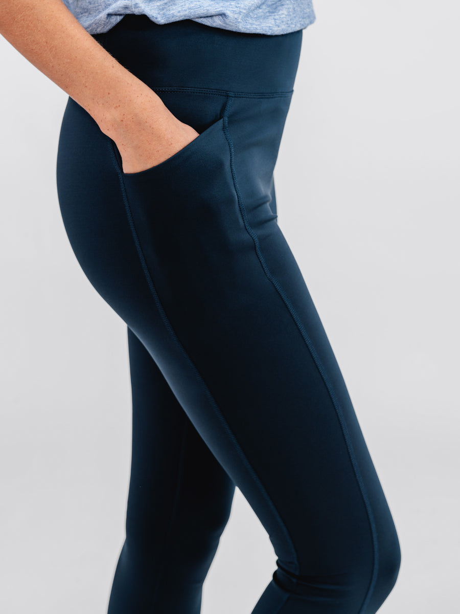 close up of model wearing navy joule active legging and chambray blue composite merino active tank with hand in pocket